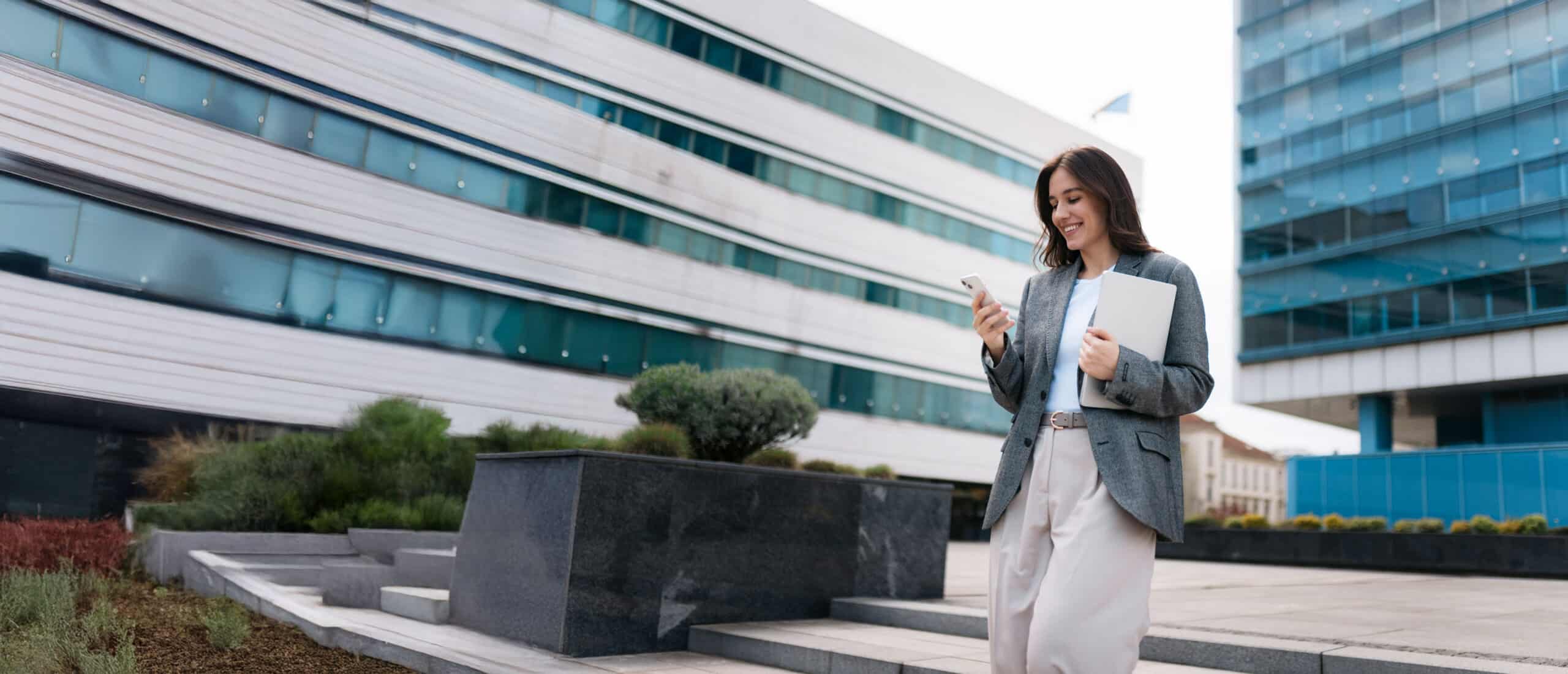A female smiling looking at her phone outside.